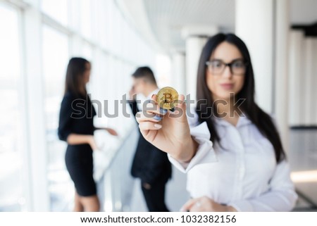 Blockchain concept. Business woman leader holding bitcoin in front of discussing team on office.