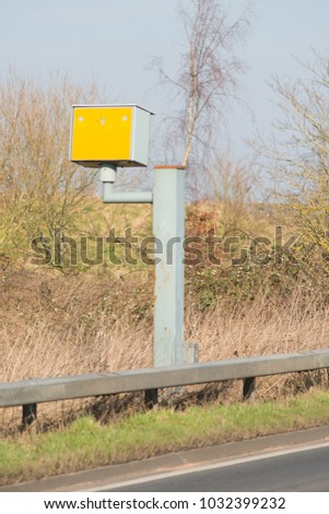 yellow gatso speed camera on roadside with typical UK countryside in background 