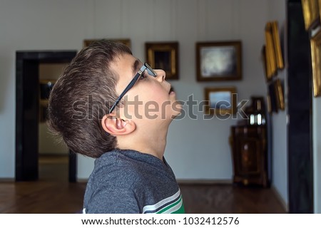 The curious and surprised boy with the glasses  looks at the pictures on the wall