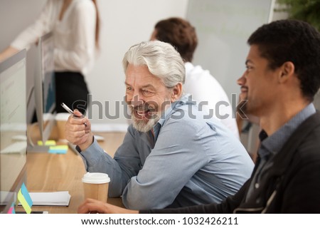 Smiling senior employee discussing email with african colleague at workplace, happy older worker talking to black coworker joking about online computer work, aged and young managers laugh in office Royalty-Free Stock Photo #1032426211