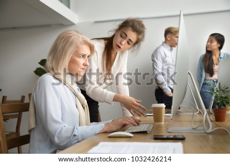 Young team leader correcting offended senior employee working on computer in office, female manager scolding aged old worker for mistake or incompetence, different generations and age discrimination Royalty-Free Stock Photo #1032426214