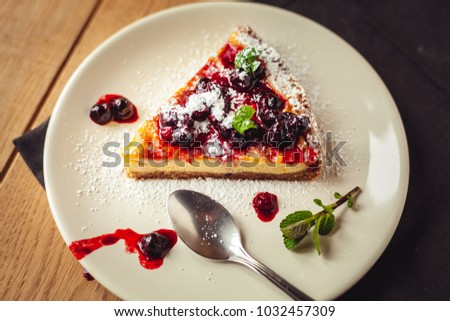 Beautiful traditional italian cheesecake with red fruits, mint, and powdered sugar on wooden background, selective focus