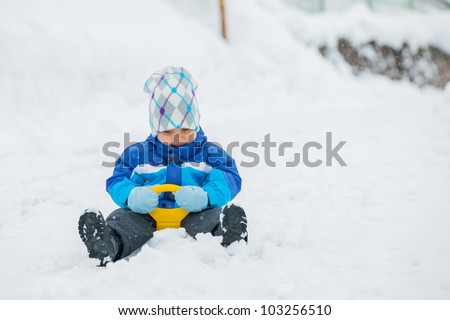 Cute little boy in blue riding on a sled near  the Austrian cottage