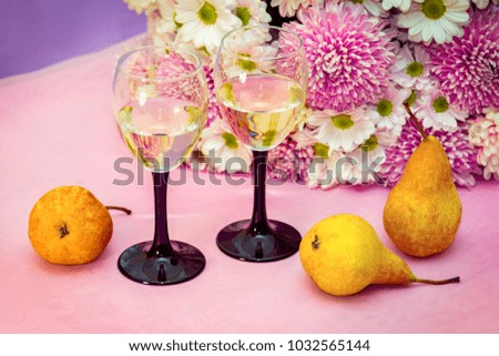 Two elegant glasses of white wine or champagne on the table with beautiful aster and chrysanthemum flowers bouquet and ripe yellow pears.