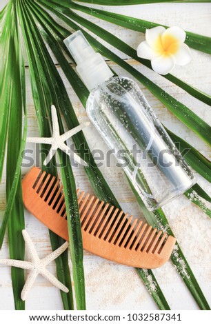 
Summer hair care. Sea salt spray water bottle top view on palm leaves with sand. 