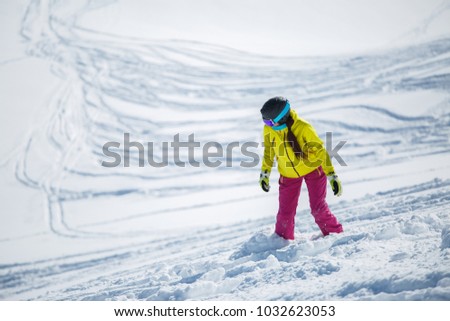 Photo of brunette wearing helmet and mask in sports clothes snowboarding from snowy mountain slope