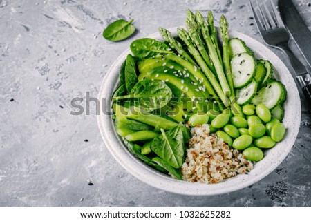 Healthy green vegetarian buddha bowl salad with fresh  vegetables and quinoa, spinach, avocado, asparagus, cucumber, edamame beans with sesame seeds on gray background. 
