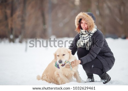 Picture of smiling woman squatting next to labrador with toy in teeth in winter park