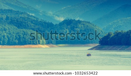 Scenic view of majectic mountain lake Vidraru with travel boat. in Carpathian mountains at Romania, wild nature landscape in the summer, panoramic view. Dramatic picturesque scene. Beautiful world.