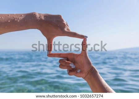 Hands show a square against the background of the sea. Close-up.