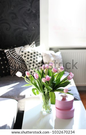 beautiful spring image of spring centerpiece on white coffee teable with pink tulips in a glass vase