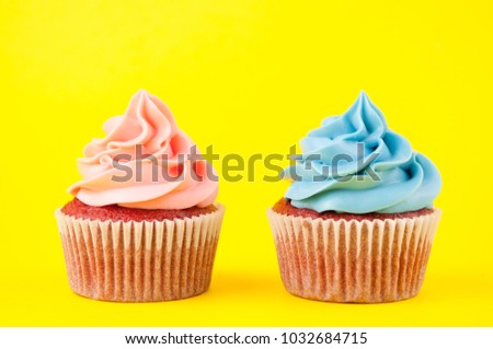 Cupcake red velvet with blue and pink whipped cream on yellow background. Picture for a menu or a confectionery catalog.