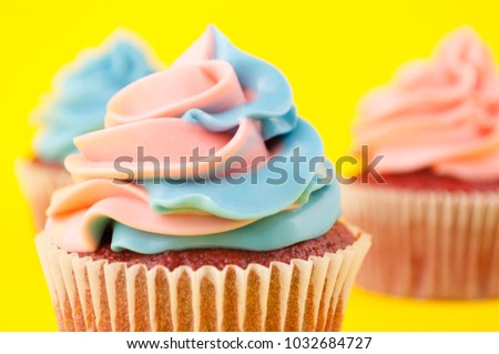 Cupcake red velvet with blue and pink whipped cream on yellow background. Picture for a menu or a confectionery catalog.