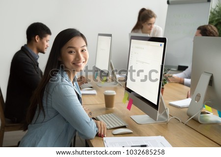 Smiling asian office employee looking at camera working with multiracial colleagues, happy young company manager sitting at corporate workplace, cheerful team member posing with desktop computer Royalty-Free Stock Photo #1032685258