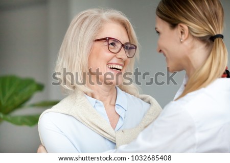 Beautiful aged woman in glasses embracing young adult lady and laughing, smiling attractive senior older mother happy to hug grown-up daughter, warm sincere family bonding having fun together Royalty-Free Stock Photo #1032685408