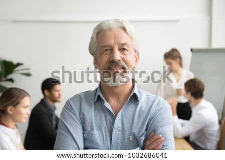 Confident senior businessman leader looking at camera with team at background, smiling aged company boss posing in office with arms crossed, older mentor or executive professional head shot portrait Royalty-Free Stock Photo #1032686041