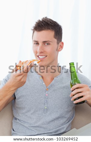 A man sitting down and smiling as he holds some beer and pizza in his hands