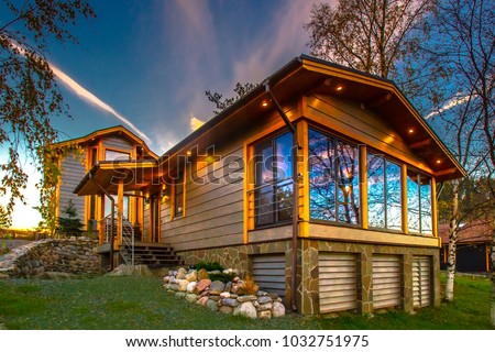 A wooden cottage with a green lawn. Cottage with panoramic windows. Glazing of cottages. Large windows in the house. Royalty-Free Stock Photo #1032751975