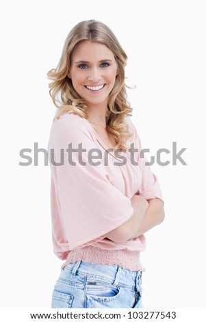 A side view shot of a woman who has her arms folded and is smiling at the camera against a white background