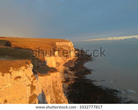 Sunset over the White Cliffs of Dover in the UK. The image shows the sun hitting the cliffs, with the higher cliffs casting a shadow to the top of the beachside cliffs.