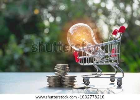 Energy saving light bulb and tree growing on stacks of coins on nature background. Saving, accounting and financial concept.