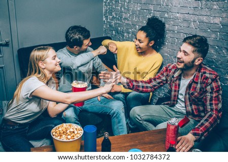A picture of young boys and girls sitting together in a small room on couches and greeting each other. They got some popcorn and ready to play some great games. Party night.