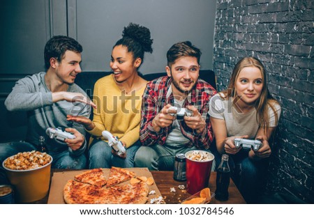 A picture where two gamers are giving low-five to each other while the other two are playing the game. All of them are enjoying time spending together.