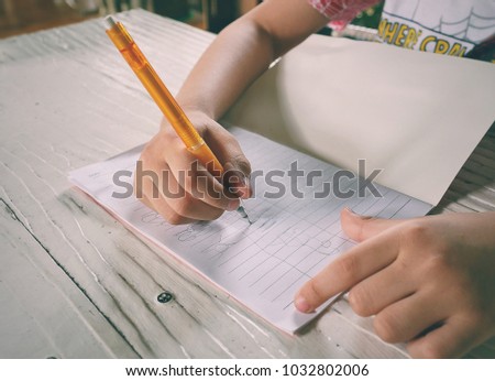 Close up of child ' s hand is drawing with a pencil  in the book on the white table.