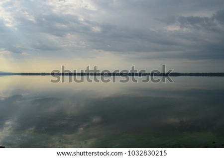 Reflexion of sky in lake, skyline landscape. Scenery of smooth, calm lake on cloudy day. Dramatic grey sky with clouds reflect in water. Water as mirror concept. Nature beauty peaceful scenery.