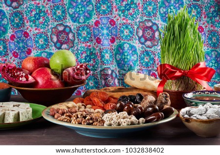 Traditional Azerbaijan sweet cuisine of holiday Nowruz: national dessert called Sumalak, lavash bread, halva, assortment of nuts and dry fruits. Sprouted seeds with red ribbon. Fresh green grass 