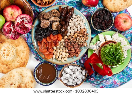 Traditional Azerbaijan sweet cuisine of holiday Nowruz: national dessert called Sumalak, lavash bread, halva, assortment of nuts and dry fruits. Sprouted seeds with red ribbon. Fresh green grass
