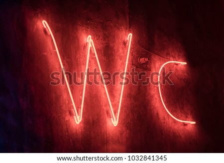 The big red letters designating a toilet executed from the neon tubes shining red light hang on a wall.