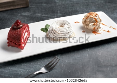 Red velvet cake, lemon cake with whipped cream and a ball of ice cream. Sweet dessert on a white plate on a wooden board.