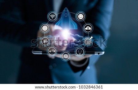 Startup concept. Businessman touching tablet and icon network connection with rocket flying out of screen on dark background Royalty-Free Stock Photo #1032846361