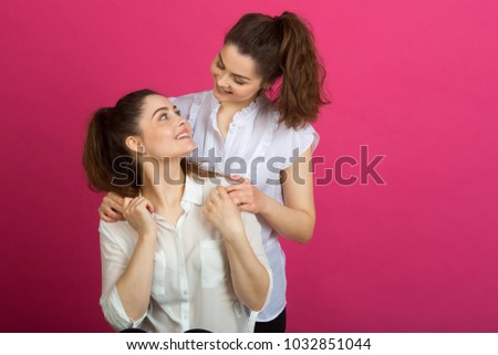 two beautiful young sisters twins in a good mood in white blouses on a pink background