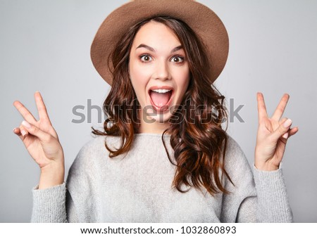 Portrait of young stylish laughing girl model in gray casual summer clothes in brown hat with natural makeup isolated on gray background. Looking at camera and showing peace sign