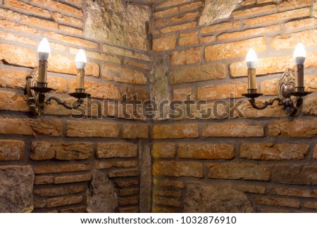 Two candlesticks with lamps in corner of brick wall in ancient building. Medieval interior. Stone and brick old house. Travel and architecture concept. Medieval decoration. Candle and candlestick.