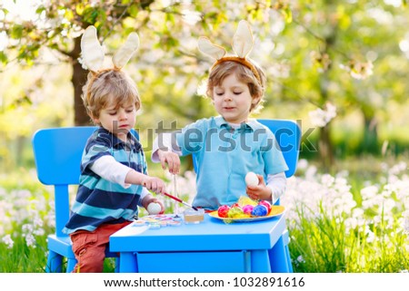 Two little boys wearing Easter bunny ears, painting colorful egg