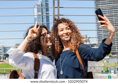 two smiling lovely girls takes a selfie with smart phone in the heart of capital city