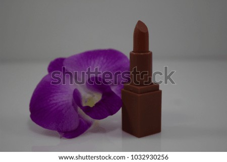 Red lipstick with purple orchid flowers on white background.