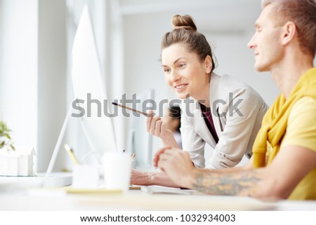 Successful businesswoman pointing at monitor display while interacting to her colleague at meeting