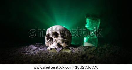 Skull and vintage hourglass on dark toned foggy background under beam of light. Horror concept. Empty space.