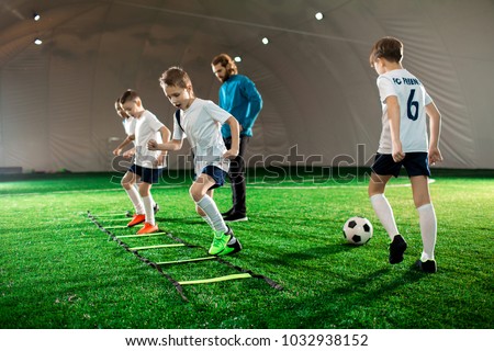 Youthful kids in uniform exercising during football training on green lawn Royalty-Free Stock Photo #1032938152