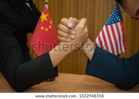 Two asian businessmen arm wrestling together on the table full of sheets of data, laptop and mobile devices,Thailand people,China vs america