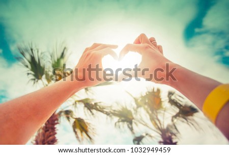 hands in heart shape framing setting sun at sunset on beach
