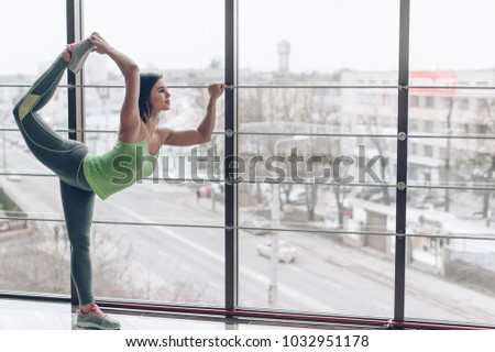 Beautiful photo of a young girl in sport standing on her hands while practicing yoga in a hall overlooking the city against the background.