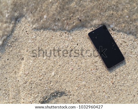 Mobile smart phone falling on the sandy beach with soft waves of sea background.
