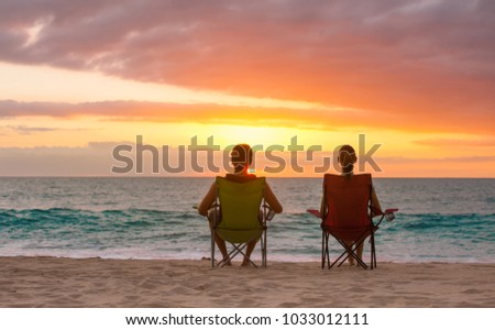 Man and woman sitting on the beach watching the sunset. Location Hawaii. 