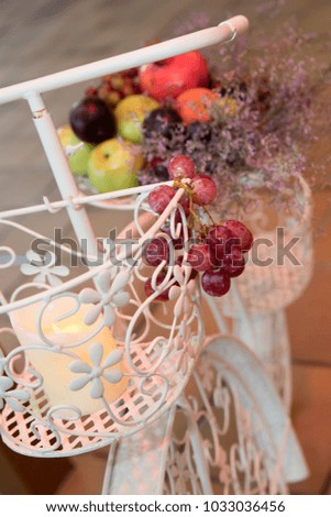 Close-up of red grapes and other fruits on background. Fruits put on white metal bicycle, candle burning in the front basket.