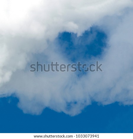 A hole in the form of a heart in a white cloud against a blue sky. A square picture. Background for design. Copy space.